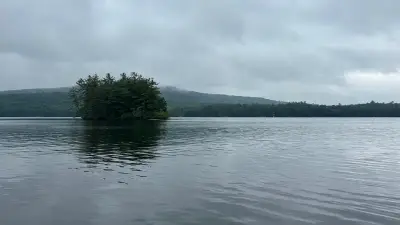 Wooded island on Crescent Lake in Raymond, Maine, beneath a cloudy sky.