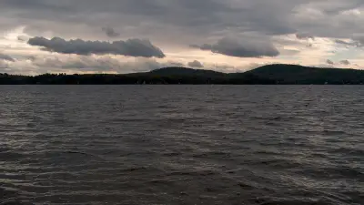 Great East Lake under a cloudy sky, viewed from the Wakefield shore toward forested hills.