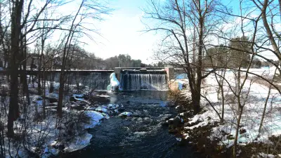 Mousam River spilling over Mill Street Dam in Springvale, with snow along the banks.
