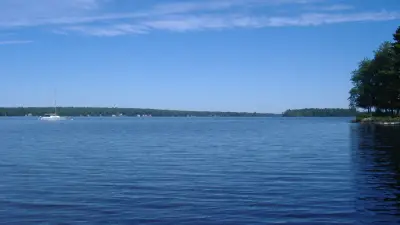 Pushaw Lake with a sailboat, low wooded far shore and wooded point to the right.
