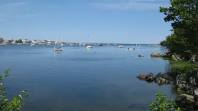 Saco River harbor with moored sailboats, shoreline homes and rocks at the University of New England bank.